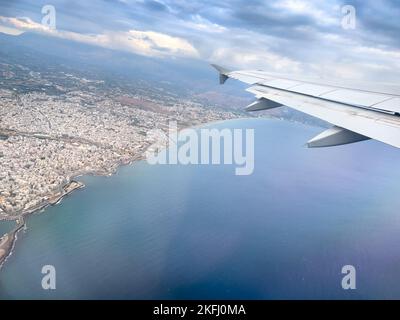 Image rognée d'une aile d'avion survolant un paysage marin et urbain contre un ciel nuageux Banque D'Images