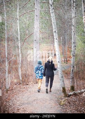 Vue arrière de la mère et du fils caucasiens randonnée sur la route de terre au milieu des arbres tout en appréciant des vacances dans les bois Banque D'Images