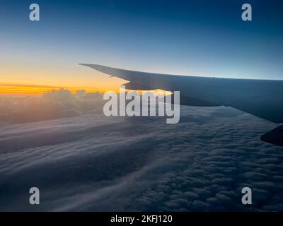 Image rognée d'un avion volant sur une vue panoramique d'un paysage nuageux moelleux au coucher du soleil Banque D'Images