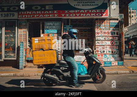 Un scooter de vélo transportant deux boîtes s'est arrêté devant une boutique de panneaux routiers grecs. Banque D'Images