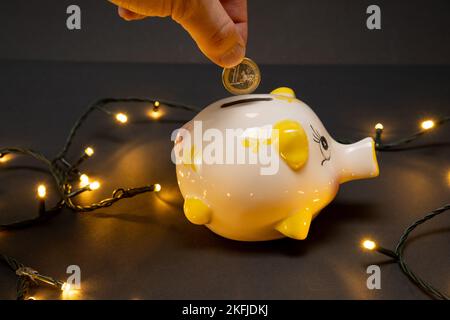 Mettre une pièce d'un euro dans une banque de porc, sur un fond sombre avec des lumières LED. Vue latérale. Le concept de noël d'économiser de l'argent. copier l'espace. Banque D'Images