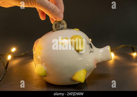 Mettre une pièce d'un euro dans une banque de porc, sur un fond sombre avec de petites lumières à DEL. Concept d'économie d'argent. copier l'espace. Banque D'Images