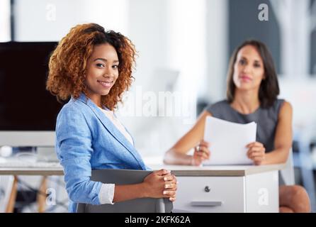 Les déménageurs et les agitateurs du bureau. Portrait de deux jeunes femmes d'affaires souriantes assises ensemble à un bureau dans un bureau. Banque D'Images