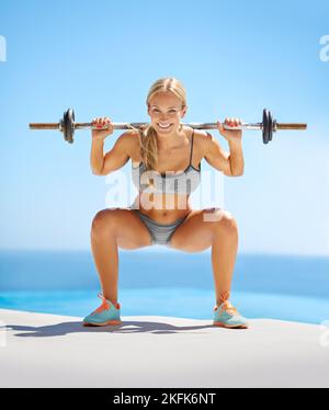 Entraînez-vous comme un champion. Portrait en longueur d'une jeune femme attrayante faisant des squats avec une barbell à l'extérieur. Banque D'Images