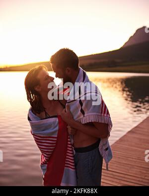 Amour au bord du lac. Jeune couple affectueux en maillots de bain enveloppés d'une serviette sur un lac. Banque D'Images