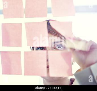 Et si je mettais cela ici... une femme d'affaires qui s'occupe de notes collantes sur un Wal en verre. Banque D'Images