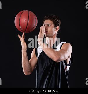 Maintenant, c'est de la compétence. Un jeune athlète fait tourner un ballon de basket-ball sur son doigt contre un fond noir. Banque D'Images