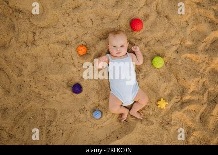 Vue de dessus d'un petit garçon heureux allongé sur une plage de sable Banque D'Images