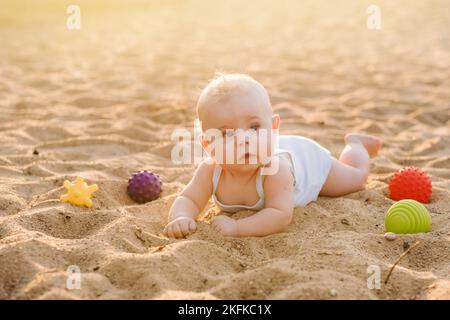 Un petit garçon heureux est couché sur une plage de sable près de la mer, aux rayons du soleil couchant Banque D'Images