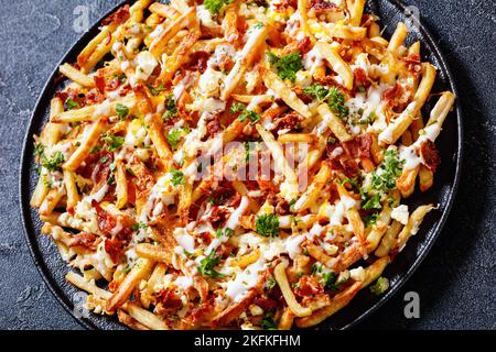 Gros plan des frites au fromage cheddar au bacon Mozzarella Feta avec sauce ranch et persil sur un plat noir sur une table en béton, cuisine américaine Banque D'Images