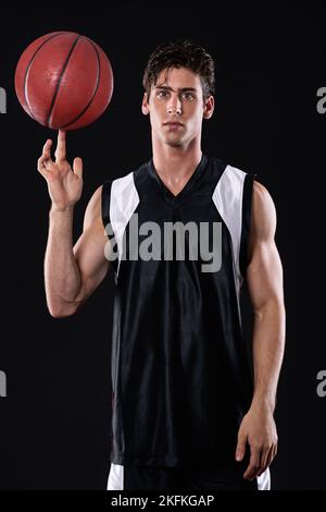 HES un homme vraiment compétitif. Portrait d'un jeune sportif qui tourne un ballon de basket sur son doigt contre un fond noir. Banque D'Images