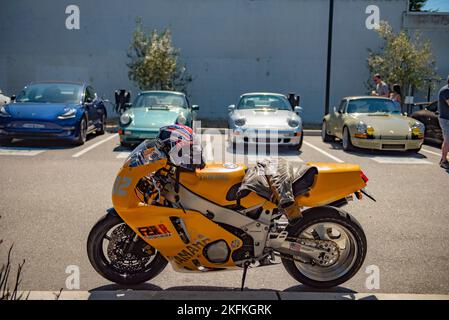 Une moto jaune FZR400 personnalisée garée devant des voitures de sport dans un parking Banque D'Images