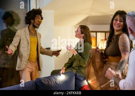 Groupe multiracial d'amis qui s'amusent, dansent et socialisent. Les adultes goûtant du vin rouge discutant et souriant lors d'une fête privée, cele Banque D'Images