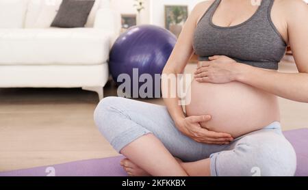 Montrant son bébé à naître un peu d'amour. Une femme enceinte s'exerçant à la maison. Banque D'Images