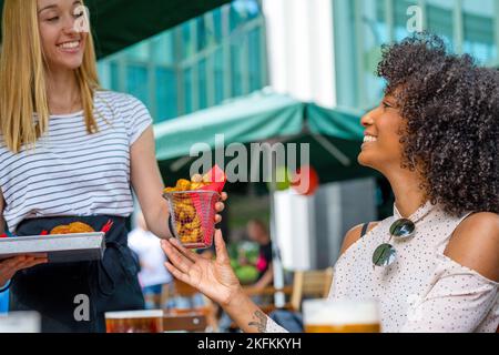 Servant de délicieux en-cas à un client, une femme afro-américaine au restaurant fast-food, en mangeant des aliments frits et en buvant de la bière Banque D'Images