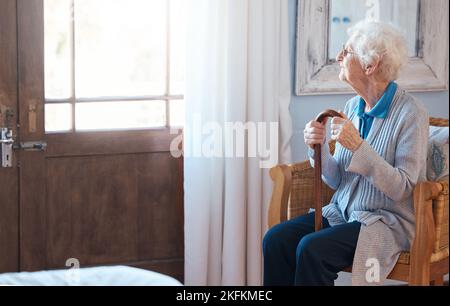 Penser, femme triste et âgée penser à la vie avec un bâton de marche près de la fenêtre dans la chambre dans une maison de retraite. Femme âgée souffrant de dépression Banque D'Images