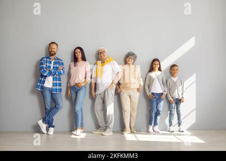 Portrait d'une famille heureuse composée de trois générations debout en ligne contre le mur gris. Banque D'Images