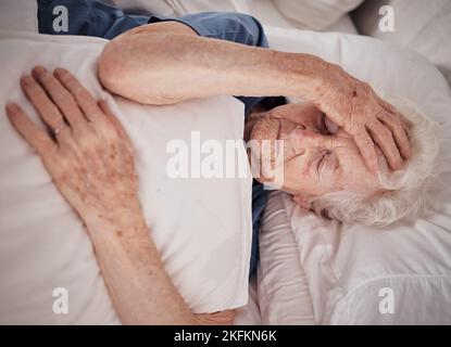 Maux de tête, douleur et femme âgée au lit pour un traumatisme de récupération, de réadaptation ou de repos dans une maison de soins aux personnes âgées. Problème de santé, urgence médicale Banque D'Images
