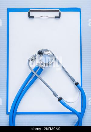 stéthoscope classique sur presse-papiers avec feuille de papier blanche vierge sur fond bleu concept médical Banque D'Images