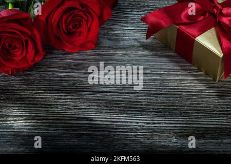 Boîte cadeau dorée roses rouges sur panneau de bois. Banque D'Images