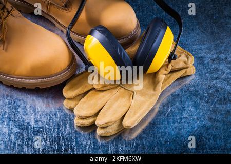 Chaussures de sécurité en cuir gants et isolation phonique protections auditives sur fond métallique rayé concept de construction. Banque D'Images