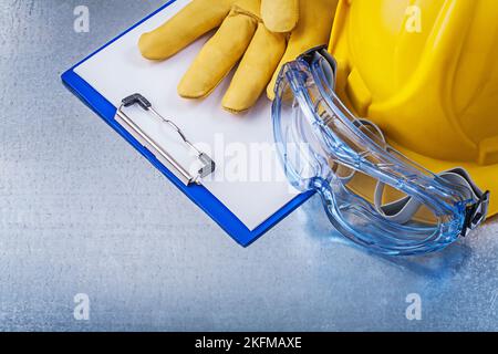 Lunettes en plastique gants de protection bloc-notes casque de construction sur fond métallique. Banque D'Images