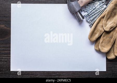 Feuille de papier clous en métal marteau et gants de sécurité en cuir sur panneau en bois vintage copier l'espace concept de construction. Banque D'Images