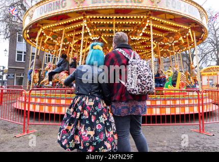 Un jeune couple britannique regardant leurs enfants sur un carrousel coloré, Ely Cambridgeshire UK. Concept: Style de vie anglais.. Banque D'Images