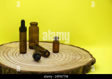 Maquette de flacons en verre brun avec couvercle compte-gouttes sur panneau en bois et sur fond jaune. Vider les flacons en verre et la pipette. Concept de soins du corps et du visage. Banque D'Images