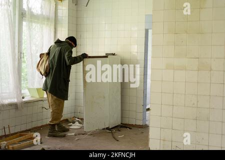 Survivant errant. L'homme va à un réfrigérateur dans un bâtiment abandonné. Post-apocalypse. Homme voyageant à pied dans un monde post-apocalyptique à la recherche Banque D'Images