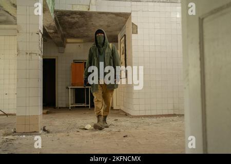 Jeune homme marchant dans un bâtiment abandonné. Homme errant. Homme dans un manteau de protection avec un capot. Post-apocalypse. Se déplacer à pied après l'apocaly Banque D'Images