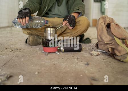 Post-apocalypse. Gros plan des mains de l'homme se trouve sur le sol d'un bâtiment abandonné qui coule de l'eau dans une tasse. Concept d'un homme qui marche dans un millepertuis post-apocalyptique Banque D'Images