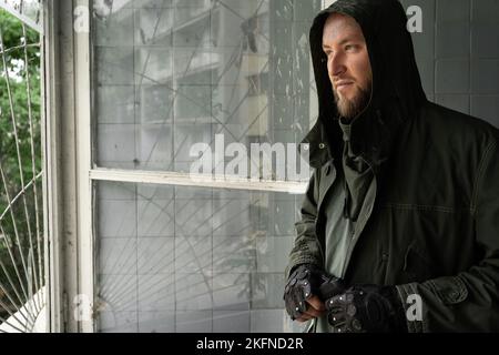 Portrait d'un soldat ou d'un tueur avec un pistolet à canon se tenir contre un arrière-plan industriel près de la fenêtre. Espace de copie vide pour l'inscription Banque D'Images