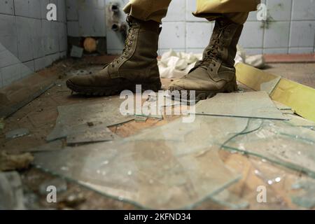 Gros plan des jambes dans les vieilles chaussures militaires sur des éclats de verre. Espace de copie. Banque D'Images