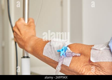 détail du bras de la femme âgée avec ligne intraveineuse tenant le pied goutte-à-goutte dans la chambre d'hôpital Banque D'Images