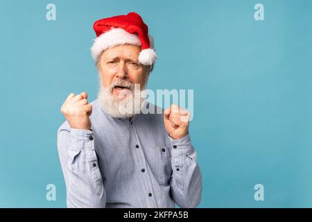 Heureux confient cool Old barbu Santa Claus vainqueur de soulever les poings célébrant le triomphe et le succès sur fond bleu avec l'espace de copie Banque D'Images