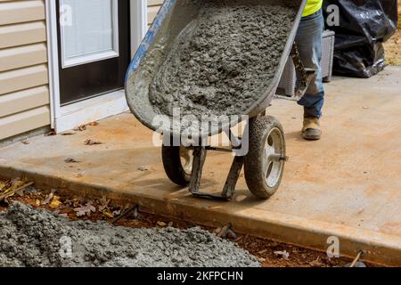 Faire un nouveau chemin de trottoir en béton près de la maison avec du ciment humide concrétisant avec le travailleur utilisant la brouette Banque D'Images