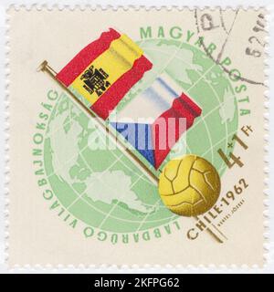 HONGRIE - 1962 21 mai: Un timbre semi-postal de 4+1 forints de vert clair et de bister représentant le Globe, le ballon de football et les drapeaux de l'Espagne et de la Tchécoslovaquie. Drapeaux aux couleurs nationales. Championnat du monde de football, Chili, 30 mai... 17 juin. Au total, 56 équipes ont participé aux phases de qualification de la coupe du monde de la FIFA 1962, se disputant un total de 16 places dans le tournoi final. Le Chili, en tant que pays hôte, et le Brésil, en tant que champions défendeurs, se sont automatiquement qualifiés, laissant 14 places ouvertes à la compétition Banque D'Images