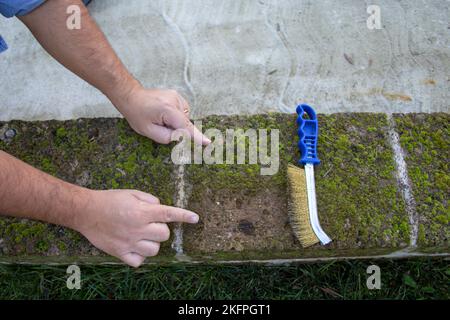 Image des mains d'un homme de main utilisant une brosse en acier pour enlever la moisissure et l'humidité des briques. Différence entre pièce propre et pièce non propre. Bricolage Banque D'Images