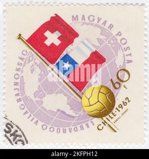 HONGRIE - 1962 21 mai: Un timbre-poste de 60 forints au lilas pâle et au bister représentant le Globe, le ballon de football et les drapeaux de la Suisse et du Chili. Drapeaux aux couleurs nationales. Championnat du monde de football, Chili, 30 mai... 17 juin. Au total, 56 équipes ont participé aux phases de qualification de la coupe du monde de la FIFA 1962, se disputant un total de 16 places dans le tournoi final. Le Chili, en tant que pays hôte, et le Brésil, en tant que champions défendeurs, se sont automatiquement qualifiés, laissant 14 places ouvertes à la compétition Banque D'Images