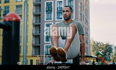 Puissant latina sportif gymnaste musclé africain américain sain homme levant les jambes sur les bars ville sport gym entraînement appuyer abs muscles. Athlète masculin Banque D'Images