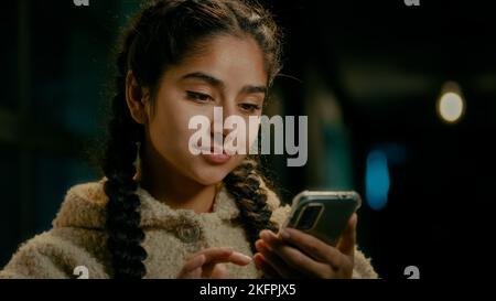 Arabian concentrée fille consommateur shopper utilisateur jeune brunette moyenne-orientale femme stand dans la ville de soir SMS messages sur le téléphone mobile gadget Banque D'Images