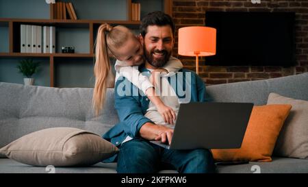 Mignonne active fille bruyante enfant joue avec papa câlins père distraire l'attention parentale dérange parent de travail sur ordinateur portable à la maison célibataire Banque D'Images