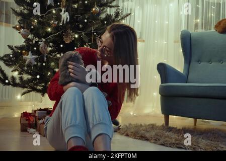 Jeune femme avec un chat assis près de l'arbre de Noël, Noël avec un chat d'animal de compagnie Banque D'Images