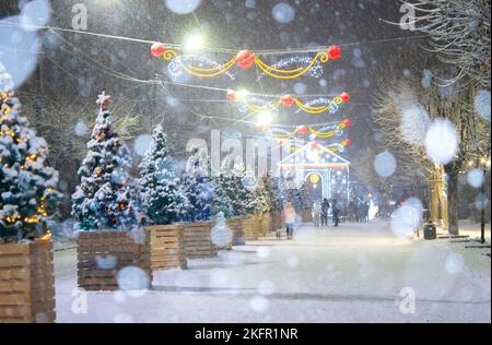 Rue de la ville pendant les chutes de neige en hiver. Beaucoup d'arbres de Noël décorés, éclairage, décoration sur la rue. Fête de Noël du nouvel an. Lanternes sur les arbres Banque D'Images