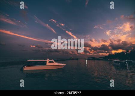 Photo à grand angle d'une jetée à côté d'une île tropicale avec un coucher de soleil spectaculaire en arrière-plan ; jetée avec plusieurs hors-bord et ferr Banque D'Images