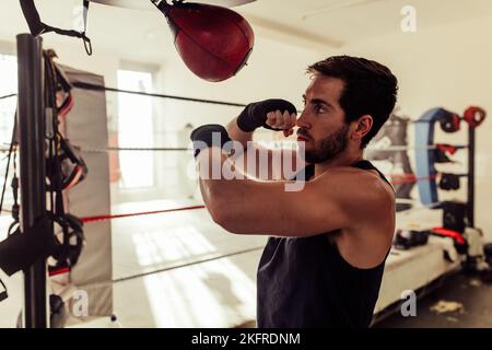 Boxeur avec une barbe frappant un sac de poinçonnage dans une salle de fitness. Un jeune sportif s'entraîner dans une salle de boxe. Banque D'Images