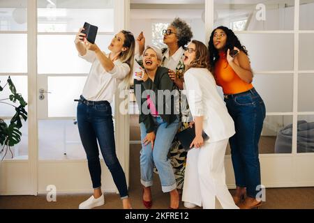 Divers hommes d'affaires font des visages drôles tout en prenant un selfie ensemble dans un bureau créatif. Groupe de gens d'affaires heureux célébrant leur succès Banque D'Images