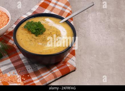 purée de soupe aux lentilles rouges dans un bol sombre avec du pain sur une table en marbre gris Banque D'Images