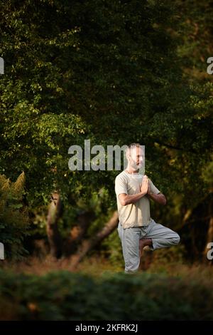 Il a trouvé un endroit tranquille de yoga. Un homme mature faisant une pose de yoga debout dans la nature. Banque D'Images